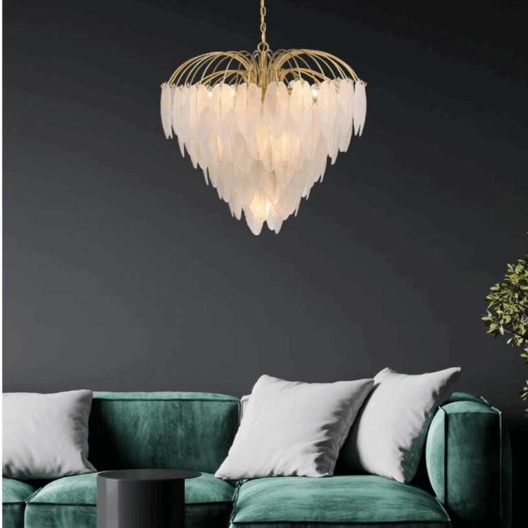 Elegant gold chandelier with layered feather-like frosted glass pieces, suspended over a green velvet sofa in a modern living room with dark walls