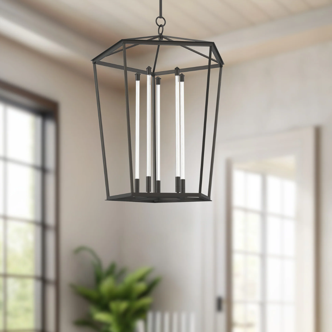 Modern black foyer pendant light with geometric open frame and vertical LED bulbs, hanging in a bright entryway with high ceilings and large windows.
