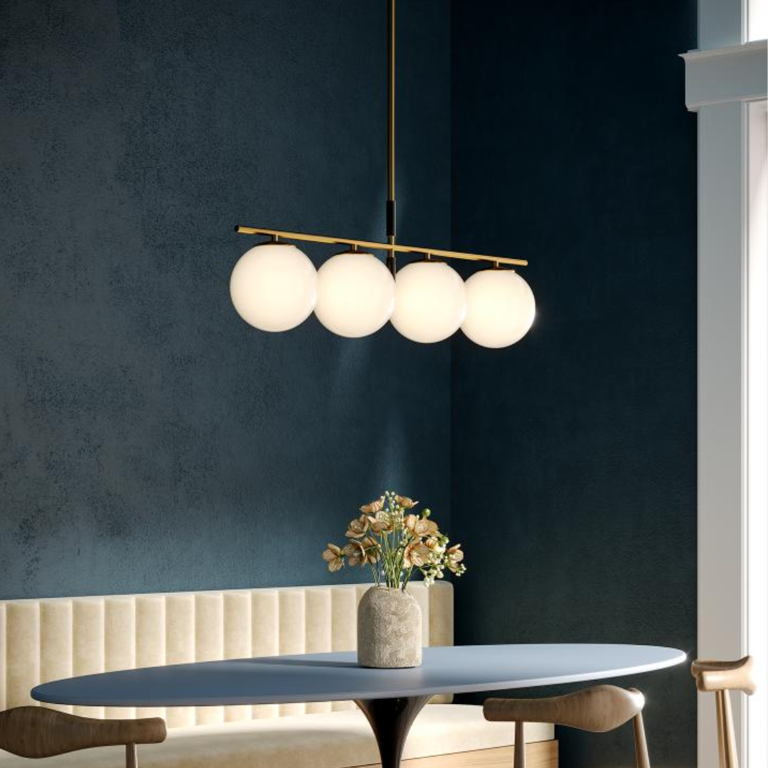 Modern linear island pendant with five frosted globe lights and a brushed gold frame, suspended above a navy blue dining nook with velvet walls and minimalist decor.