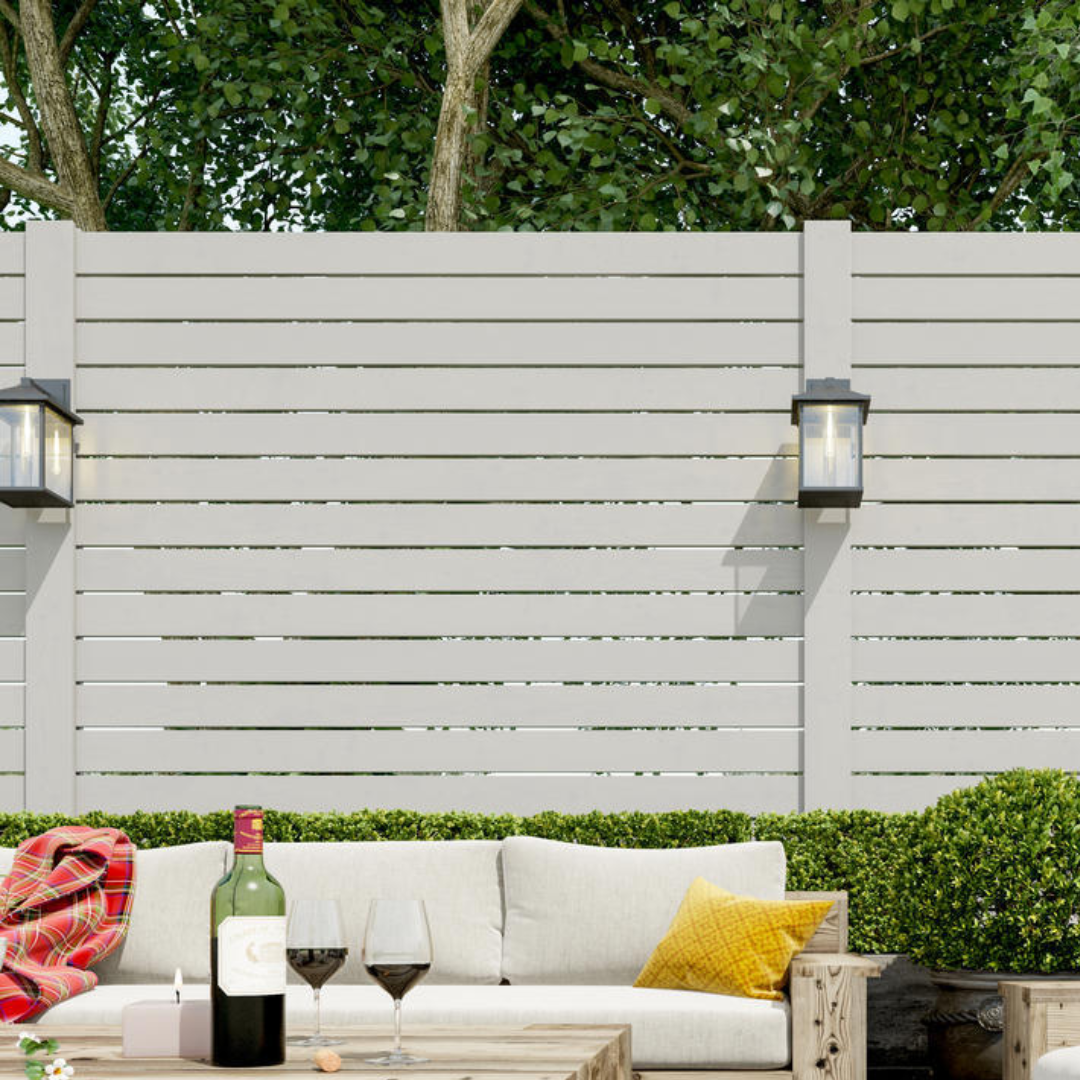Modern black outdoor wall lanterns mounted on a white privacy fence, illuminating a cozy patio lounge with wine, pillows, and greenery in the backgroun