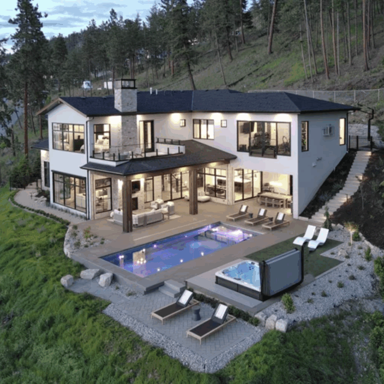Modern luxury hillside home with large windows, contemporary exterior lighting, infinity pool, and hot tub surrounded by lush greenery at dusk.