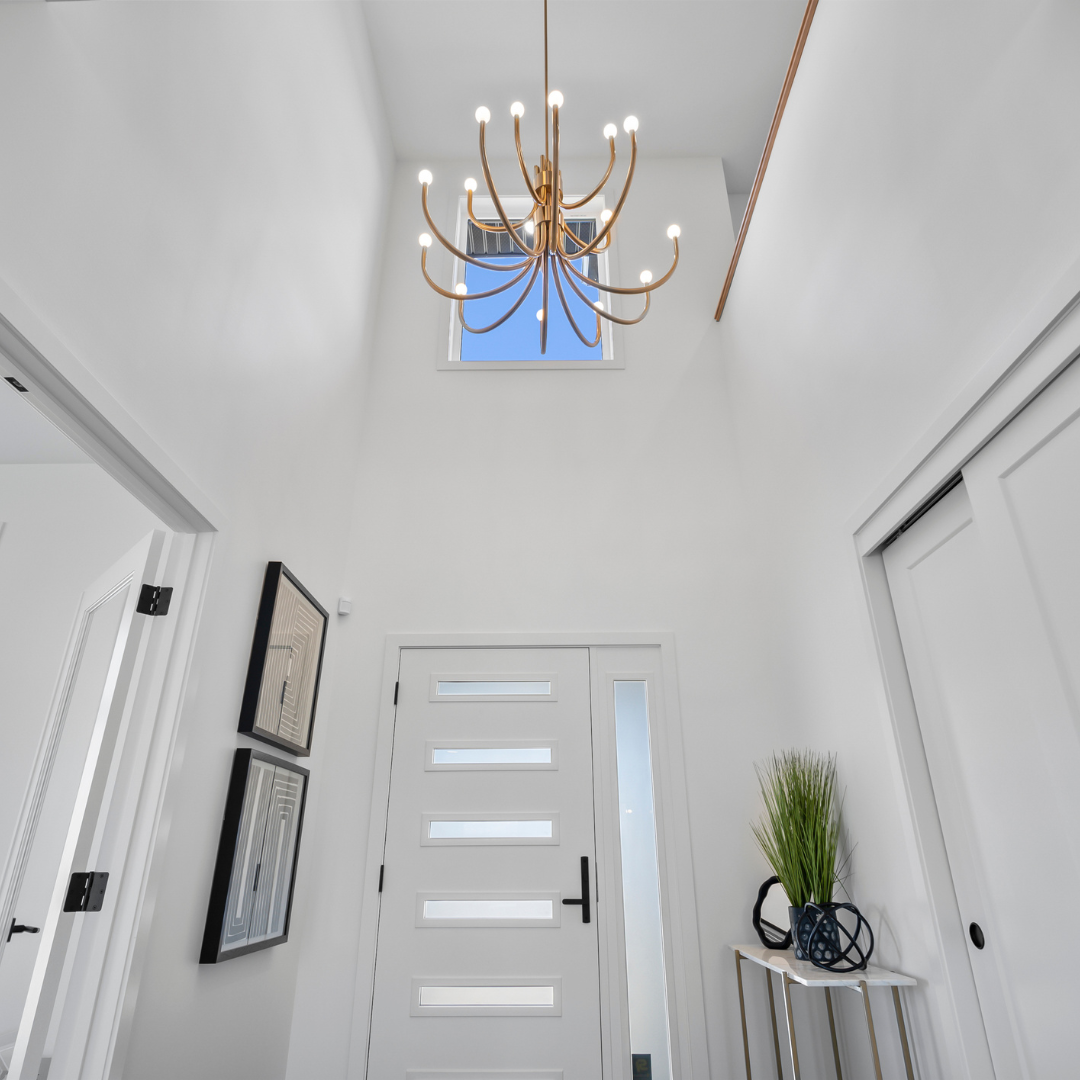 Modern white entryway with tall ceiling, gold multi-arm chandelier, and contemporary front door with horizontal glass inserts
