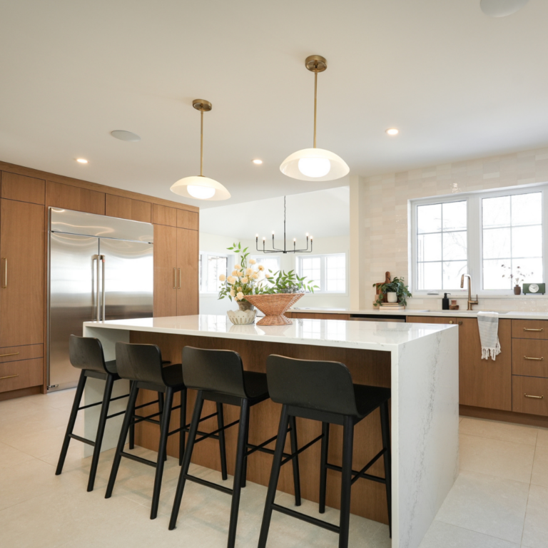 Modern Winnipeg kitchen with warm wood cabinetry, large waterfall island, black bar stools, and contemporary pendant lighting above the island.