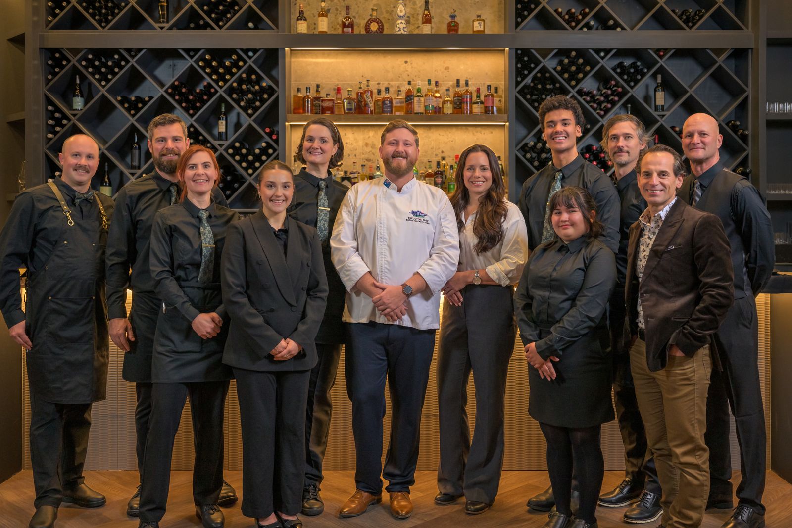 Team photo inside Kettle Valley Steakhouse at Big White Ski Resort featuring luxury restaurant lighting and illuminated wine display wall.