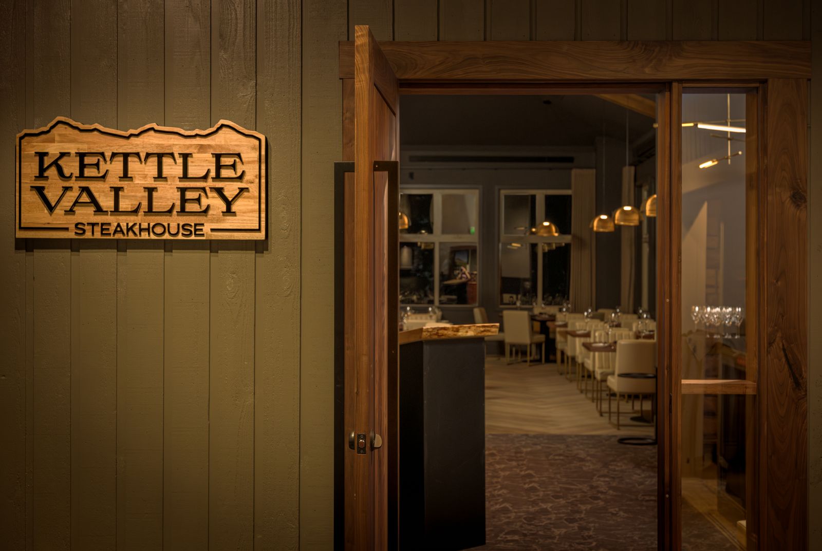 Entrance signage and interior lighting at Kettle Valley Steakhouse in Big White Ski Resort showcasing warm luxury hospitality lighting.